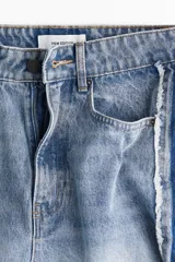 Jean de tiro alto, confeccionado en denim de algodón rígido, de corte ancho y pierna recta. Presenta un lavado celeste claro con efecto desgastado en el centro y franjas laterales en denim más oscuro con acabado desflecado.