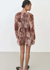 Vestido corto de gasa semitransparente con estampado animal print en tonos marrones. Presenta cuello redondo con detalle fruncido, mangas largas con puños elásticos y volantes decorativos en la parte superior y en el ruedo. Incluye forro interior.