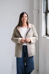 Tapado de paño con capucha, color beige, con cierre frontal, bolsillos laterales y puños vueltos en tono más claro.
