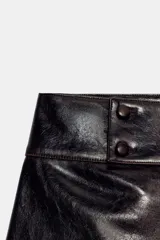 Shorts de tiro medio con efecto de cuero brillante en color negro, con cierre frontal y detalles de botones en la cintura.