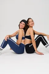 Conjunto deportivo compuesto por un top de escote cuadrado y calzas largas de tiro alto con diseño cruzado en la cintura. Ambas piezas son de color azul con detalles de ribetes blancos en los bordes y laterales. El top cuenta con el logo de la marca estampado en el frente.