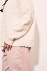 Sweater color crema con motas de colores, de corte oversize, cuello redondo y mangas largas.