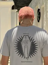 Remera gris de manga corta con corte regular, de la marca Kaboa Industries, con estampa en la espalda que presenta un esqueleto dentro de un ataúd rodeado por alas oscuras y las leyendas WAKE UP y Kaboa Industries.