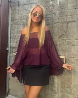 Top tipo poncho de gasa transparente en color violeta oscuro, con diseño de hombros descubiertos y mangas amplias tipo murciélago.