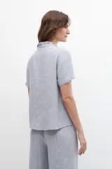 Blusa celeste de lino con cuello mao con volados, mangas cortas y cierre frontal con botones.