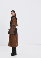 Chaqueta larga tipo trench color marrón, con diseño recto, solapas anchas, doble botonadura, bolsillos laterales y cinturón desmontable de la misma tela.
