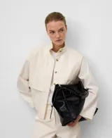 Camisa de mujer color crudo, de corte recto, con cuello chimenea abotonado y manga larga con abertura. Presenta botonadura frontal y bolsillos de plastrón con logo bordado en el pecho.