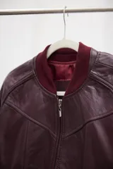 Campera tipo bomber de cuero ovino color marrón oscuro, con cuello de tejido acanalado y cierre frontal con cremallera.