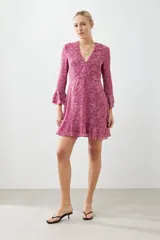 Vestido corto fucsia con estampado floral, escote en V, mangas largas con volados y falda acampanada con volados en el ruedo.