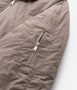 Campera bomber masculina de poliamida, con cuello, puños y ruedo de tejido elástico. Presenta cierre frontal con cremallera, dos bolsillos laterales con solapa y botón, y un pequeño bolsillo con cierre en una de las mangas.