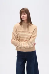 Sweater de punto color beige con rayas horizontales color crema, cuello alto y corte holgado. Presenta costuras decorativas en hombros y pecho.