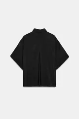 Camisa de corte fluido confeccionada en mezcla de modal, con cuello solapa, manga corta con dobladillo y bolsillo de plastrón en el delantero. Presenta cierre frontal con botones ocultos por tapeta y aberturas laterales en el bajo.