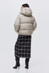 Campera puffer color beige con capucha, cierre frontal y solapa con botones a presión. Cuenta con bolsillos laterales, elástico en los puños y cordón ajustable en la capucha y el ruedo.