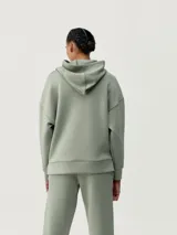 Buzo con capucha color verde, de tejido técnico, diseño holgado, hombro caído y bolsillos.