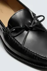 Mocasín de vestir fabricado en piel con acabado brillante, presenta un detalle de lazo en el empeine y suela a contraste con ligero tacón.