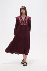 Vestido midi holgado de viscosa color vino tinto, con mangas largas y volados en los hombros. Presenta un canesú con bordado floral en tonos rosados y cuello con abertura en forma de lágrima y lazo para atar.