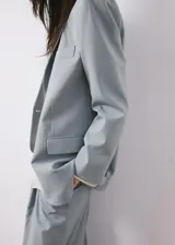 Blazer de corte sastrero en color gris azulado, con cierre frontal de un botón, solapas clásicas y bolsillos laterales con solapa.