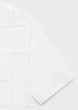 Camiseta blanca de algodón con diseño calado geométrico, corte recto y mangas cortas.