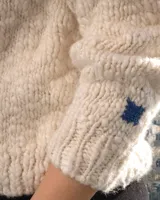 Sweater de cuello redondo tejido a mano en dos agujas, confeccionado en una mezcla de lana merino y seda. Presenta un diseño de punto grueso con detalle de bordado artesanal en color azul.