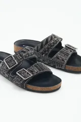 Sandalia baja abierta de estilo 'slide' con dos tiras ajustables con hebillas metálicas. Las tiras están completamente decoradas con bordados de mostacillas, canutillos y strass en tonos negros y grises. La plantilla es de corcho visible forrada en cuero negro, y la suela es de goma.