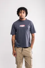 Remera gris con estampado frontal de la marca Atomic en rojo y blanco. Corte boxy fit.