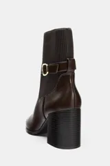 Botín de tacón alto en bloque, con cuerpo de cuero sintético y caña de tejido acanalado. Presenta una tira decorativa con hebilla metálica en el tobillo y acabado en punta.