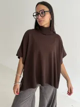 Poncho de tejido de punto color marrón chocolate, con cuello alto tipo polera y mangas cortas amplias. Presenta un diseño holgado con terminaciones acanaladas en el ruedo.