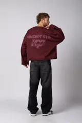 Buzo de cuello redondo confeccionado en tejido rústico con bordes al corte y costuras expuestas. Presenta un diseño boxy con estampado frontal y es reversible, permitiendo su uso por ambos lados.