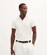 Camisa polo de manga corta confeccionada en algodón, con cuello en V y detalles en color contrastante en el cuello y los puños. Presenta un diseño de tejido en media malla, ofreciendo una textura suave y transpirable.