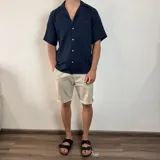 Camisa de hombre color verde oliva, de muselina con textura arrugada, manga corta, corte oversize, cuello cubano y cierre con botones. Presenta un pequeño logo bordado en el pecho.