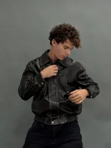 Campera estilo bomber de cuero sintético con efecto desgastado, cuello camisero, cierre frontal con botones a presión y puños y cintura elásticos.