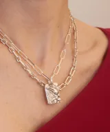 Collar de plata con cadena de eslabones tipo clip y dije rectangular texturizado con detalles en relieve y piedras verdes incrustadas.