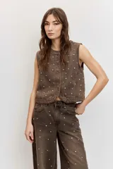 Chaleco de denim marrón con efecto acid wash y apliques de strass distribuidos por toda la prenda, sin mangas y con cierre frontal de botones.