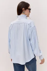 Camisa celeste con cuello alto, volados frontales y mangas largas con puños ajustados.