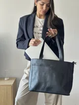 Cartera tipo tote de cuero graneado negro, con diseño clásico y textura uniforme. Cuenta con doble asa de hombro, bolsillo frontal con cierre magnético, bolsillo trasero con cierre metálico y compartimento principal con cierre. El interior está forrado y dispone de múltiples bolsillos organizadores.