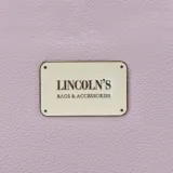 Billetera larga con cierre perimetral, confeccionada en material sintético texturizado color mostaza. Cuenta con correa de mano extraíble y placa metálica con logo de la marca en el frente.