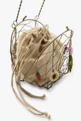 Bolso rígido con estructura metálica dorada y forro interior de tela color beige ajustable con lazada. Decorado con charms colgantes de diferentes motivos y asa superior rígida.