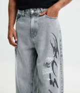 Pantalón de jeans para hombre, modelo super baggy, color celeste desgastado, con estampa de grafiti en negro en ambas piernas. Presenta cintura con trabilla, cierre tradicional y bolsillos.