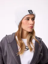 Gorro tipo beanie de punto acanalado en color lila, con parche rectangular negro en el frente que incluye la inscripción 'EAT THE WAVE'.