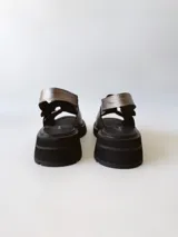 Sandalias de cuero color peltre con plataforma y suela track color negro. Presentan dos tiras anchas con hebillas plateadas y tira trasera ajustable.