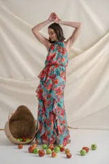 Vestido largo de gasa de seda natural con estampado floral en tonos verde y rojo. Tiene corte en la cintura, falda con volados y tajo delantero.