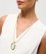 Conjunto de joyería compuesto por un collar largo con cadena tipo cola de ratón y un dije ovalado con piedra central verde agua y marco de metal martillado, acompañado por un par de aros tipo argolla pequeña.