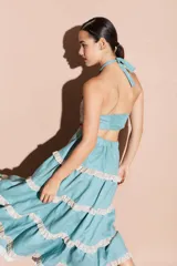 Top halter con acabado brillante, escote alto y detalles de ojalillos decorativos en los bordes. Diseño con espalda descubierta y cierre ajustable.