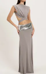 Set de dos piezas color gris, compuesto por un top drapeado sin mangas con tiras cruzadas en la cintura y una falda larga de tiro bajo con pretina de lentejuelas plateadas.