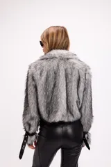 Campera de pelo sintético negro con detalles en cuero sintético, bolsillos frontales con solapa y cinturón ajustable con hebilla metálica.