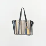 Bolso tipo tote con cuerpo a rayas verticales en tonos beige, blanco y negro. Laterales y asas de cuero sintético negro. Incluye un dije de borlas colgando de una de las asas.