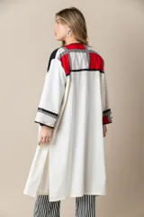 Túnica larga color marfil con vivos negros de satén, bolsillos laterales y diseño geométrico con bloques de color rojo y negro.