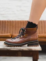 Borcego de cuero color marrón con detalles en cuero con textura de cocodrilo en el talón y aplique de gamuza en el lateral. Tiene cordones negros, herrajes metálicos y suela track con doble costura.