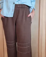 Pantalón de algodón color arena, de corte recto y holgado, con cintura elástica y detalle de costuras horizontales decorativas en la parte inferior de las piernas.