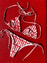 Bikini de dos piezas con estampado geométrico en rojo y blanco. El corpiño es tipo triángulo con tiras ajustables para anudar en cuello y espalda. La bombacha es regulable lateralmente con tiras anudables.